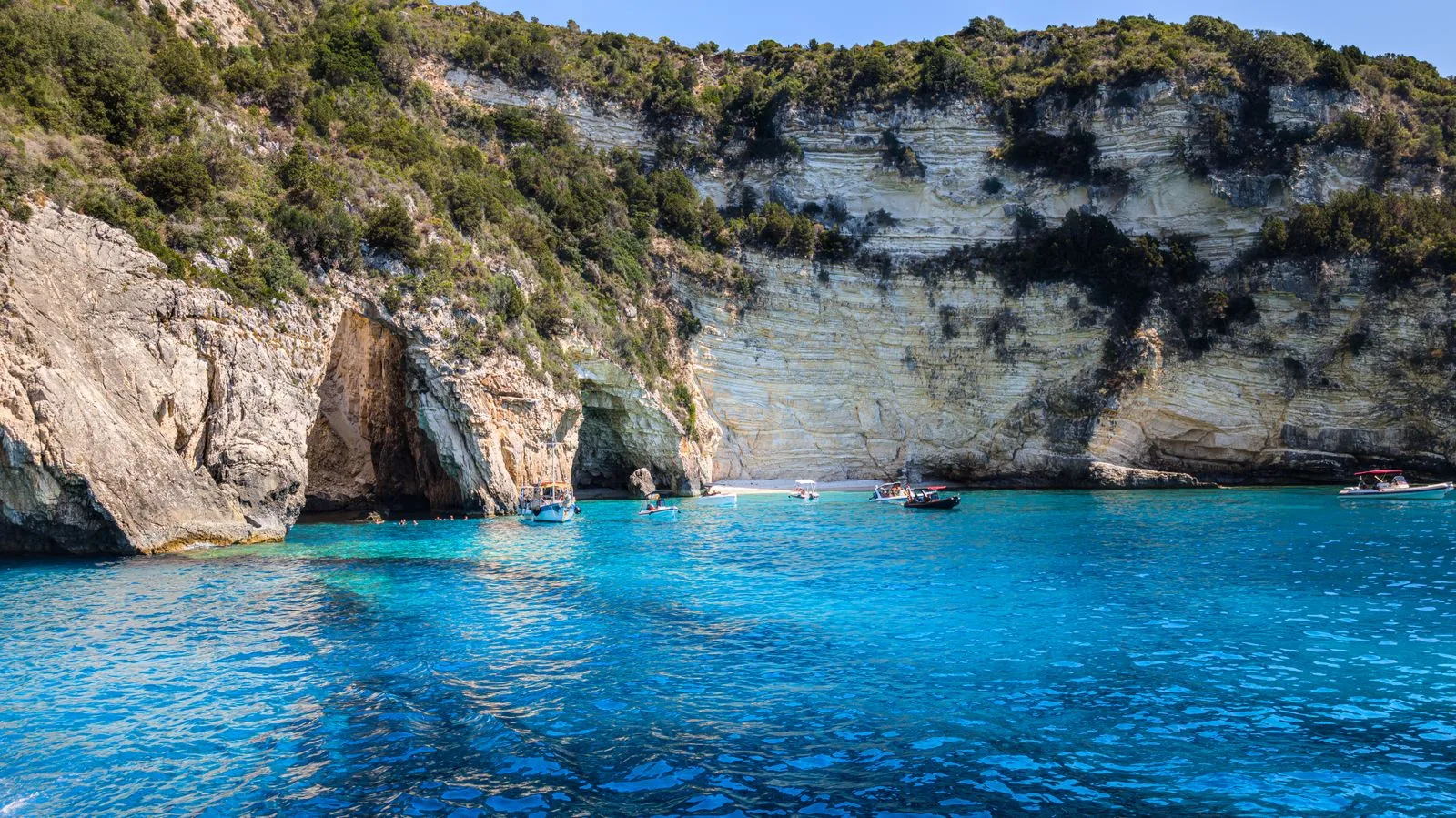 Boats on vibrant blue water near rocky cliffs, similar to the Blue Caves boat trip in Zakynthos
