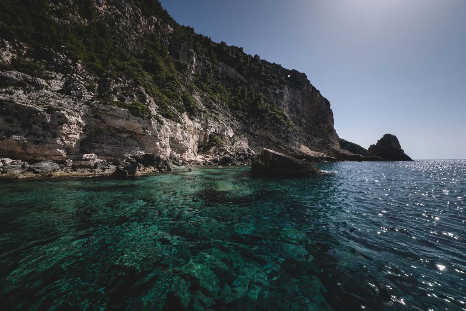 A rocky cliff meeting turquoise sea under a bright sky, typical of western Zakynthos coves