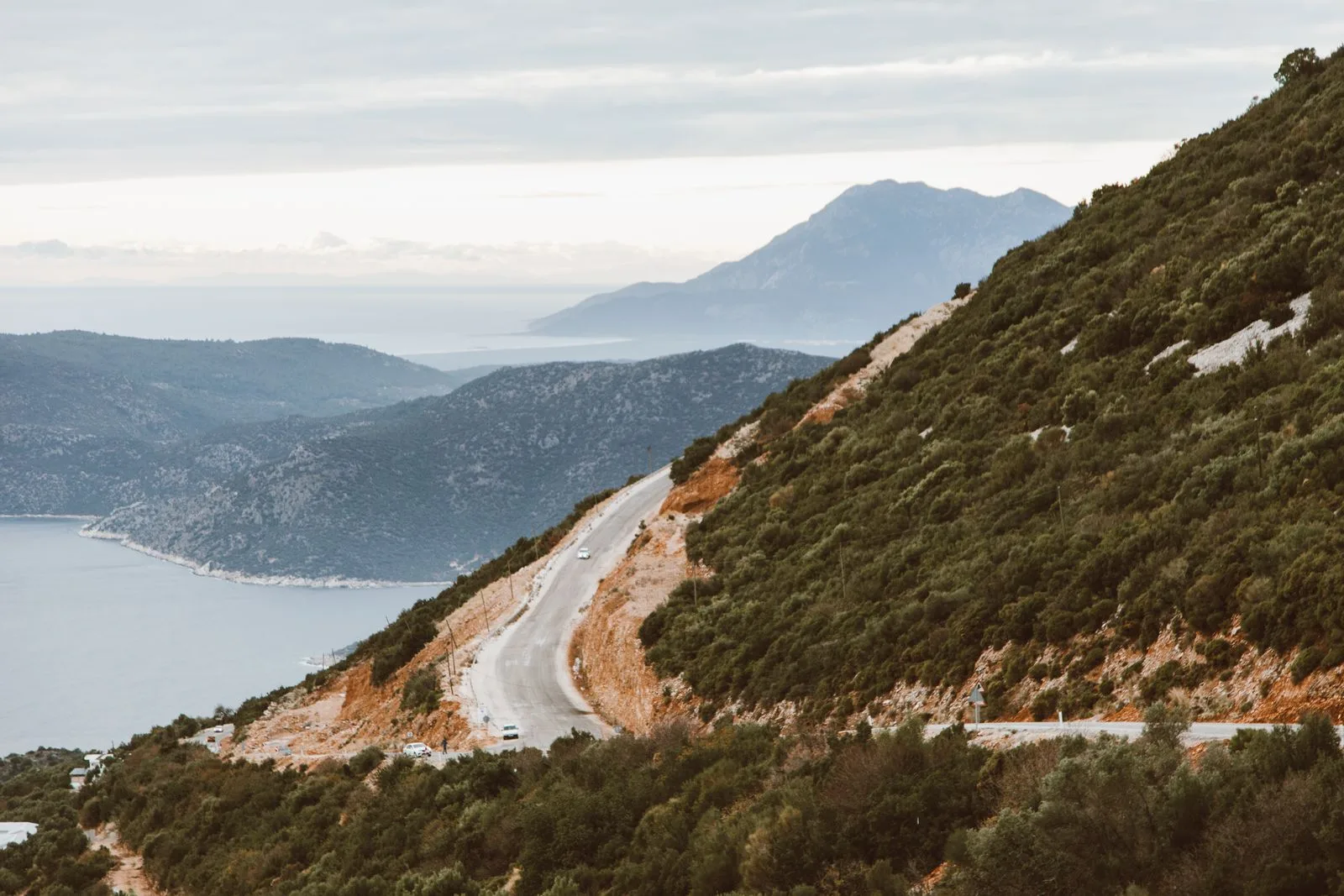 A winding coastal road through hills with ocean views, similar to the drive to Porto Limnionas